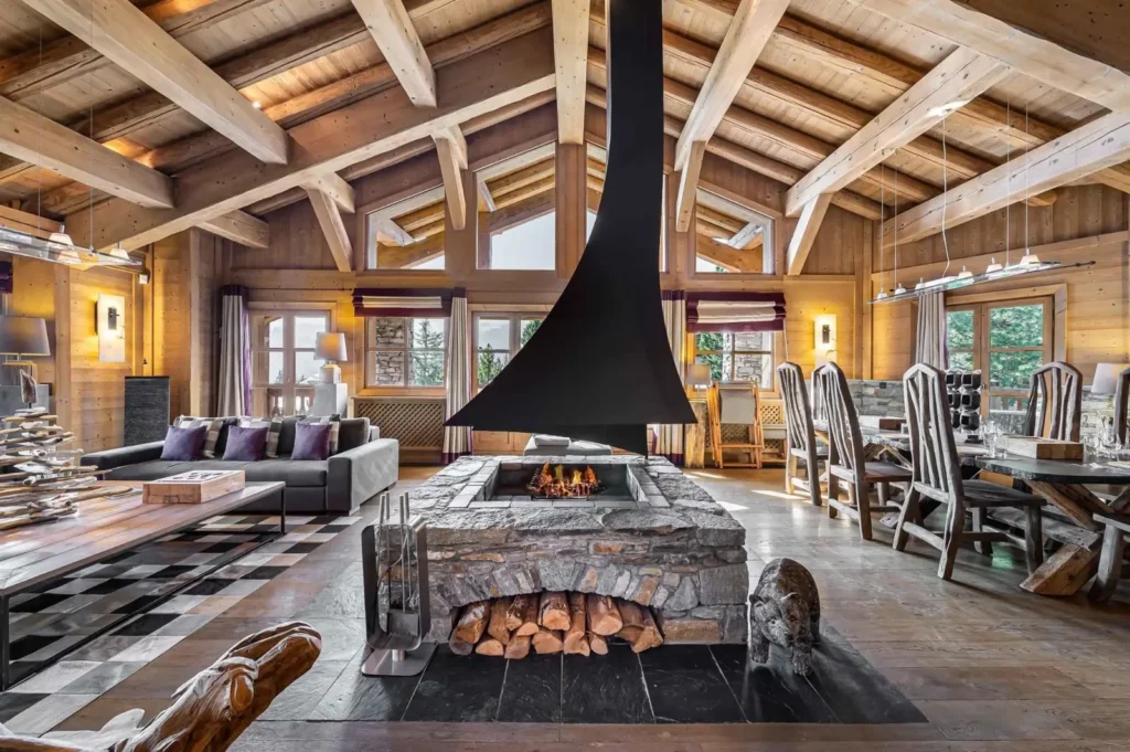 Living room with a central suspended fireplace and exposed beams at Chalet Biollay, a chalet for 10 guests in Courchevel 1850