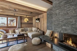 Lounge with a grey stone fireplace, a corner sofa and knitted poufs at Apartment Campanule in Saint-Martin-de-Belleville