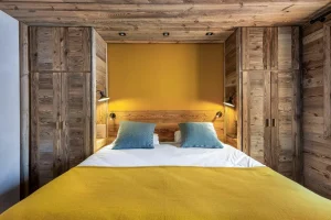 Double bedroom with the bed framed by reclaimed-wood wardrobes and a yellow headboard at Apartment Campanule in Saint-Martin-de-Belleville
