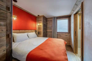Double bedroom with an orange headboard and a window onto the mountain at Apartment Campanule in Saint-Martin-de-Belleville