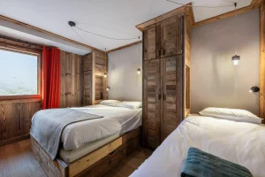 Bedroom with a double bed, a single bed and a red curtain at the window at Apartment Campanule in Saint-Martin-de-Belleville