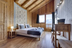 Bedroom under exposed beams with a desk and balcony facing the peaks, at Apartment des Eucherts