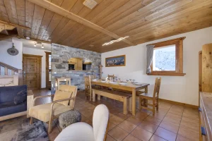 Dining area with a large wooden table, a stone wall and the lounge beyond, at Apartment des Eucherts