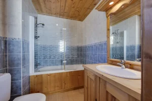 Bathroom under a sloping ceiling with a bathtub and washbasin, at Apartment des Eucherts