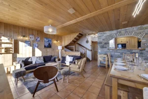 Living area under a timber ceiling with lounge, staircase and a laid dining table at Apartment des Eucherts in La Rosière