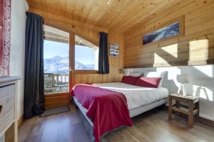 Double bedroom with a red bedspread and a window onto the mountain, at Apartment des Eucherts
