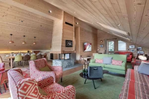 Lounge of Apartment Rhodos in Méribel with patterned armchairs, a green sofa, a central fireplace and the dining area beyond