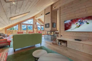 Lounge with a TV, a ski poster and the central fireplace opening onto the large windows at Apartment Rhodos