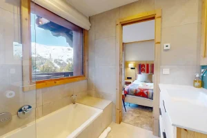 En-suite bathroom with a bathtub and a window onto the mountains, with the bedroom visible beyond, at Apartment Rhodos