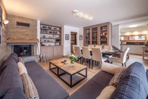 Lounge with a stone fireplace, grey sofas and the dining room beyond at Chalet Alisier in Méribel Village