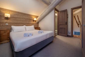 Double bedroom under the roof beams with light wood panelling at Chalet Alisier in Méribel Village