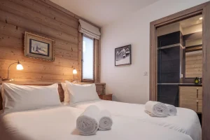 Bedroom with two single beds pushed together, wood panelling and a bathroom at Chalet Alisier in Méribel Village