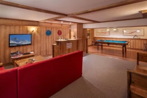 Relaxation lounge with a red sofa, a TV, a bar and a pool table at Chalet Alisier in Méribel Village