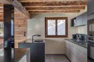 Equipped kitchen with a black island, an extractor hood and a window onto the snow at Chalet Arnica in Les Saisies