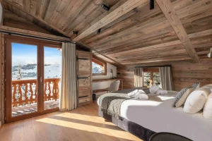 Bedroom under the roof beams with a large bed and a French door onto the balcony at Chalet Arnica in Les Saisies