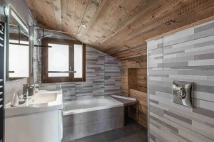 Bathroom under a sloping ceiling with a bathtub and a washbasin at Chalet Arnica in Les Saisies