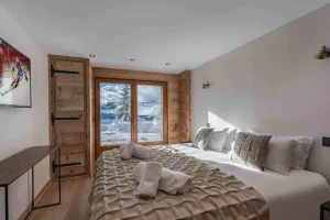 Bedroom with a large bed, a wall-mounted TV and a French door at Chalet Arnica in Les Saisies