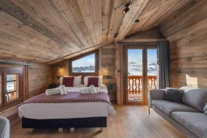 Attic bedroom with a bed, a sofa and balcony access at Chalet Arnica in Les Saisies