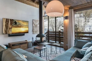 Lounge with a black suspended fireplace, blue-grey sofas and a wall-mounted TV at Chalet Bouleau in Méribel