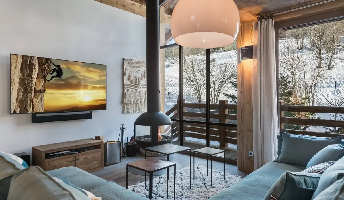 Lounge with a black suspended fireplace, blue-grey sofas and a wall-mounted TV at Chalet Bouleau in Méribel