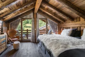 Bedroom under exposed beams with a fur-covered bed and balcony access at Chalet Bouleau in Méribel