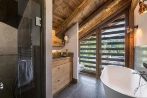 Bathroom under the roof beams with a freestanding bath, a basin and a shower at Chalet Bouleau in Méribel