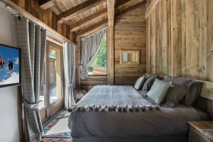Bedroom with a double bed, checked curtains and a French door onto the balcony at Chalet Bouleau in Méribel