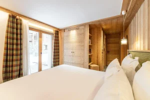 Double bedroom with tartan curtains, a French door and a red headboard at Chalet Brigues in Courchevel Le Praz