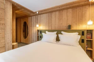 Double bedroom with a white bed, wood panelling and a green headboard at Chalet Brigues in Courchevel Le Praz