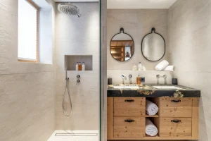Bathroom with a walk-in shower, a black stone double washbasin and round mirrors at Chalet Brigues in Courchevel Le Praz