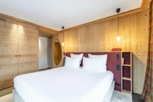 Double bedroom with a white bed, tartan curtains and light wood panelling at Chalet Brigues in Courchevel Le Praz