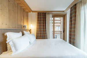Double bedroom with checked curtains, balcony access and a white bed at Chalet Brigues in Courchevel Le Praz