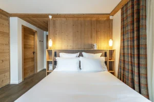 Double bedroom with light wood panelling, a headboard and a tartan curtain at Chalet Brigues in Courchevel Le Praz