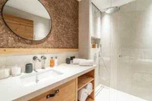 Bathroom with a wooden unit, a round mirror and a glass shower at Chalet Brigues in Courchevel Le Praz
