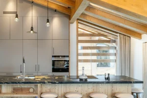 Contemporary kitchen with a black stone central island and stools at Chalet Brigues in Courchevel Le Praz
