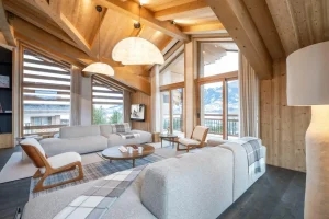 Lounge under exposed beams with grey sofas, wooden armchairs and large picture windows at Chalet Brigues in Courchevel Le Praz