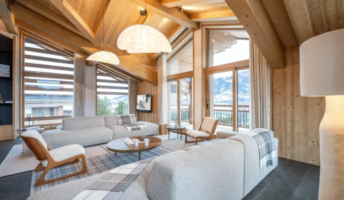 Lounge under exposed beams with grey sofas, wooden armchairs and large picture windows at Chalet Brigues in Courchevel Le Praz