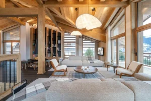 Bright lounge with sofas, armchairs and a round coffee table, with a bookcase beyond at Chalet Brigues in Courchevel Le Praz