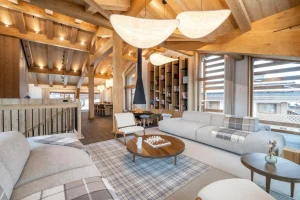 Spacious living area with lounge, central fireplace and bookcase under the roof beams at Chalet Brigues in Courchevel Le Praz