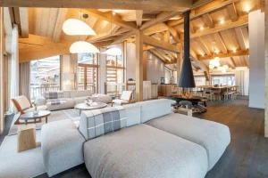 Living area with a corner sofa, a suspended central fireplace and the dining room at the back at Chalet Brigues in Courchevel Le Praz