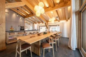 Dining room with a long wooden table, chairs and the open kitchen at Chalet Brigues in Courchevel Le Praz