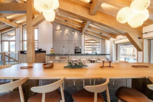 Solid wood dining table under designer pendant lights, with the open kitchen at Chalet Brigues in Courchevel Le Praz