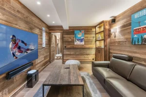 Separate TV lounge with a leather sofa, a large screen and ski posters at Chalet du Plantin in Méribel Village