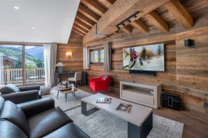 Lounge with leather sofas, a red armchair, a wall-mounted TV and a glazed door onto the balcony at Chalet du Plantin in Méribel Village