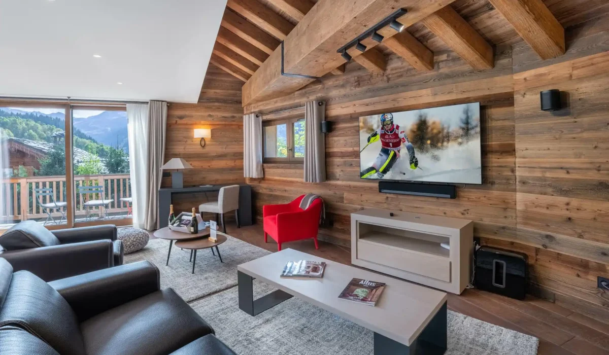 Lounge with leather sofas, a red armchair, a wall-mounted TV and a glazed door onto the balcony at Chalet du Plantin in Méribel Village