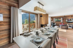 Dining room with a large laid table and a black glazed partition opening onto the kitchen at Chalet du Plantin in Méribel Village