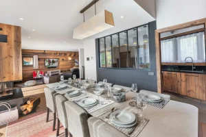 Dining room with a table for twelve, a large window onto the mountains and the lounge beyond at Chalet du Plantin in Méribel Village