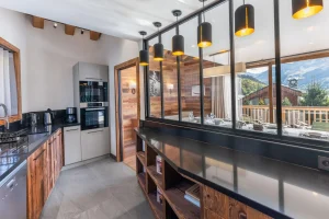 Modern equipped kitchen with a built-in oven, black counter and glazed partition onto the living area at Chalet du Plantin in Méribel Village