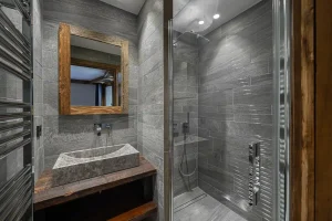 Grey stone shower room with a stone washbasin and a wood-framed mirror at Chalet du Plantin in Méribel Village