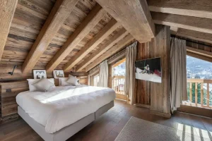 Master bedroom under the roof beams with a double bed and a mountain view at Chalet du Plantin in Méribel Village